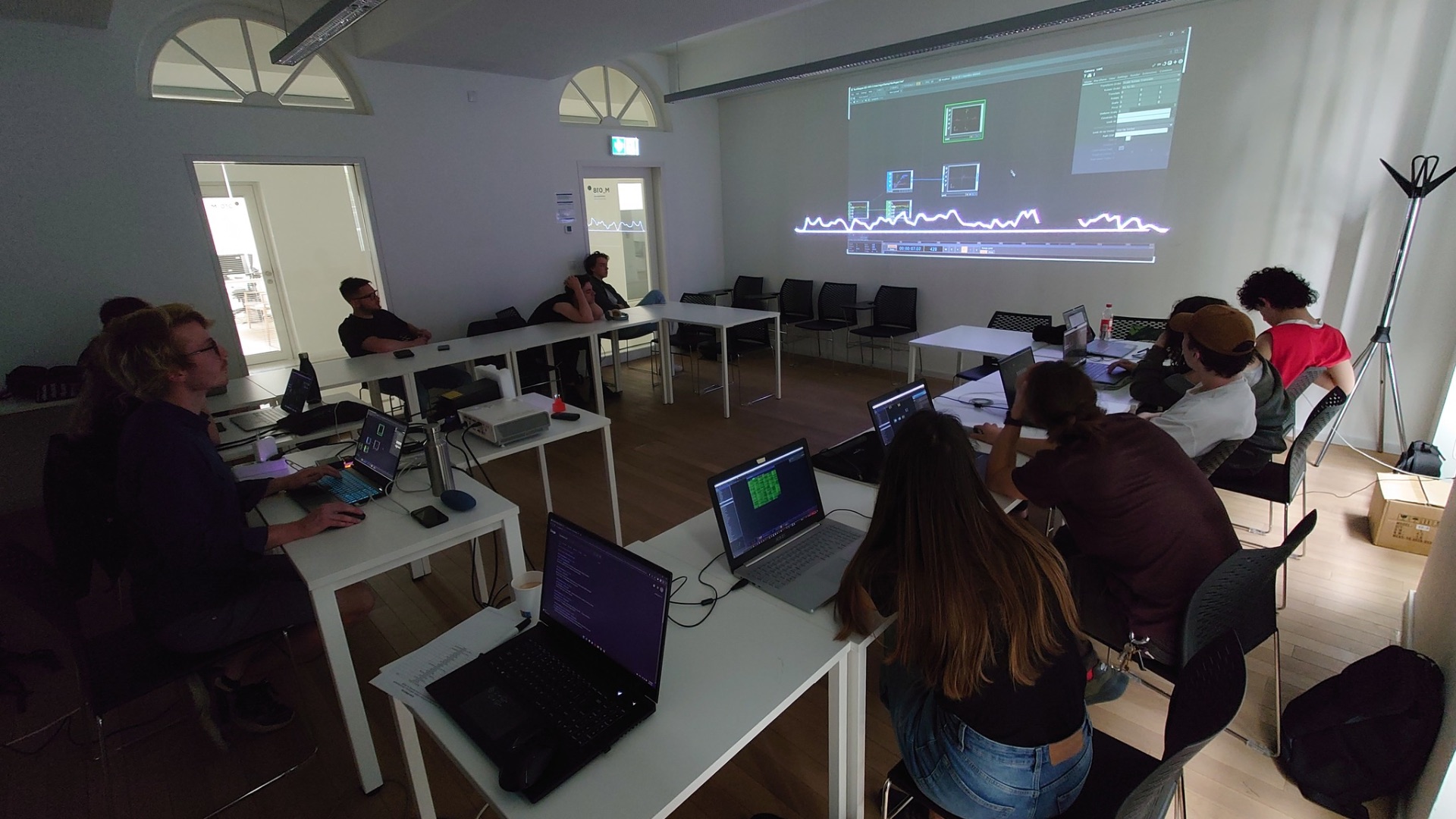 Workshop room with projected TouchDesigner network and laptops